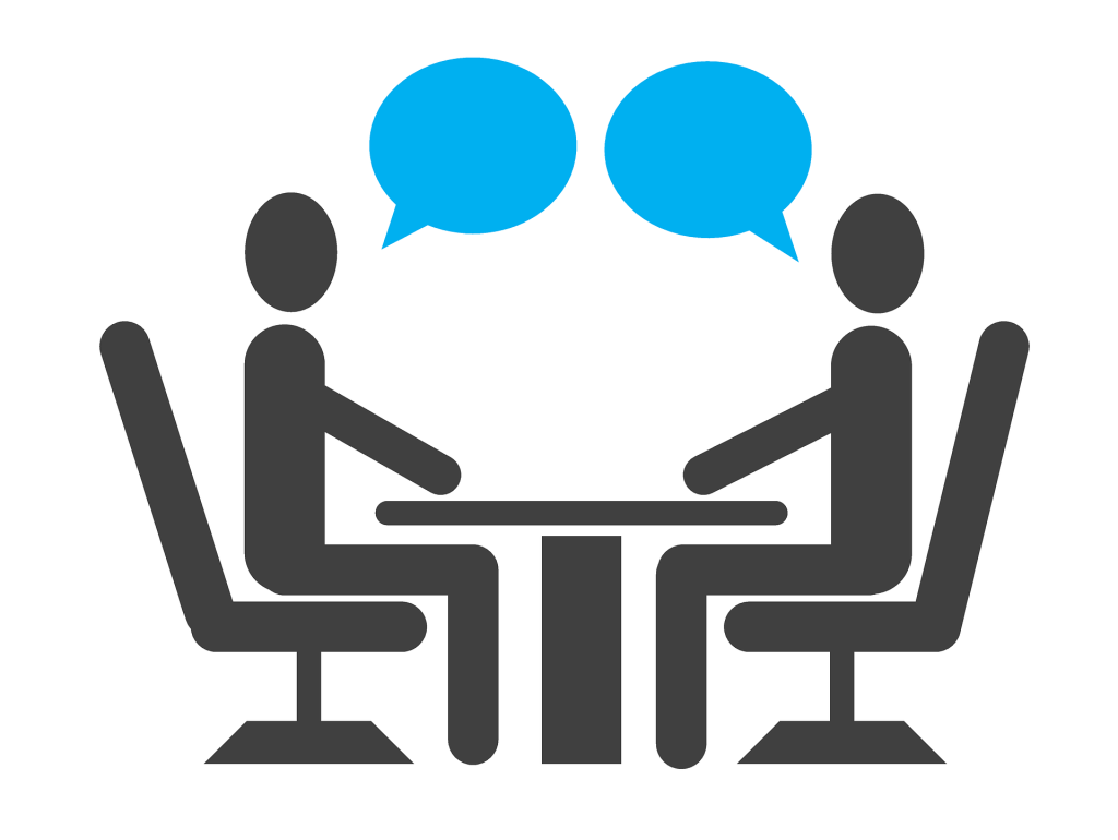 Stick figure silhouette of two people sitting at a small table with two blue and conversation bubbles between them.