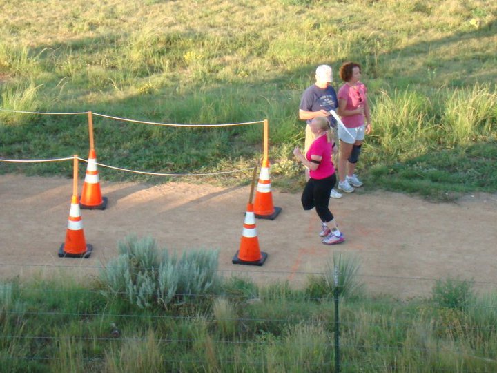 Author photographed crossing the finish line on a dirt trail with two individuals in the background.